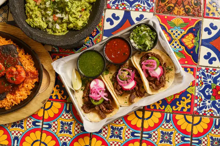 Tacos with salsas and guacamole on a colorful tiled table